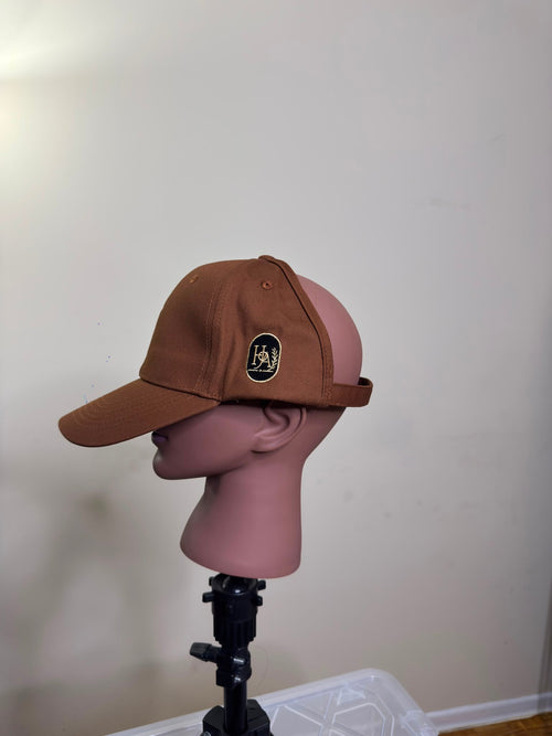Side view of the House of Adjeh backless baseball cap showing the navy and gold crest